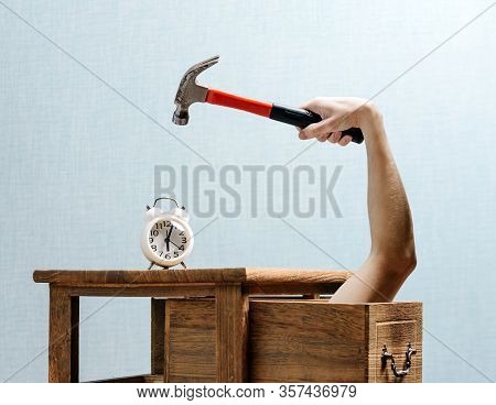 The Alarm Clock Stands On The Bedside Table, A Hand With A Hammer, Lifted Above The Alarm Clock, Is 