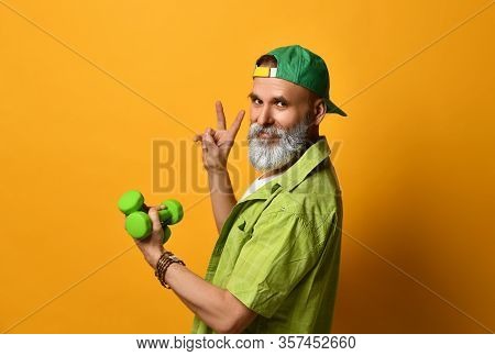 Gray-bearded Male In Green Cap And Shirt, White T-shirt, Bracelet. Smiling, Showing Victory Hand, Ho