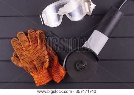 Grinder, Gloves And Safety Glasses On A Black Wooden Table. View From Above.