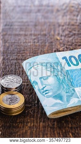 Several Coins Of Money Of Brazil And Many Notes Of 100 Reais. Rustic Wooden Background, Concept Of P