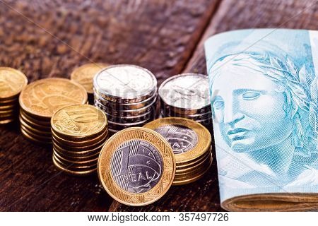 Several Coins Of Money Of Brazil And Many Notes Of 100 Reais. Rustic Wooden Background, Concept Of P