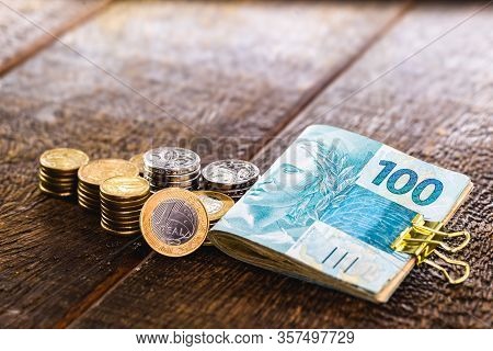 Several Coins Of Money Of Brazil And Many Notes Of 100 Reais. Rustic Wooden Background, Concept Of P
