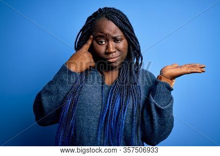 African american plus size woman with braids wearing casual sweater over blue background confused and annoyed with open palm showing copy space and pointing finger to forehead. Think about it.