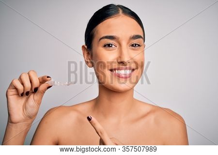 Young beautiful brunette woman holding dental aligner orthodontic to teeth corretion very happy pointing with hand and finger