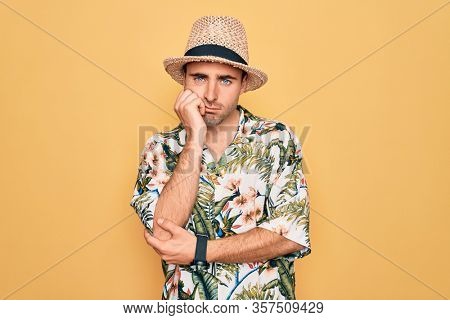 Young handsome man with blue eyes on vacation wearing summer florar shirt and hat thinking looking tired and bored with depression problems with crossed arms.