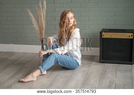 Young Beautiful Woman With Bare Feet Sitting On The Floor Next To Subwoofer And Glass Vase With Dry 