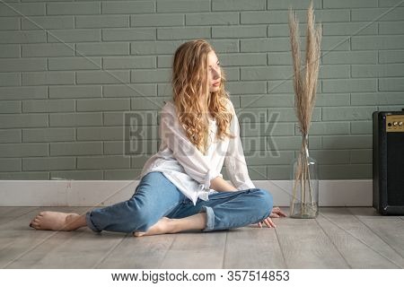 Young Beautiful Woman With Bare Feet Sitting On The Floor Next To Subwoofer And Glass Vase With Dry 
