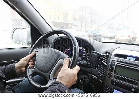 Men's Hands On The Steering Wheel Of A Car. The Driver Controls The Car. View Through The Windshield