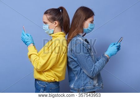 Profile Of Two Focused Attractive Young Females Standing Back To Back Isolated Over Blue Background 
