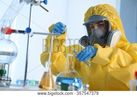 Scientist In Chemical Protective Suit Dripping Reagent  Into Test Tube At Laboratory. Virus Research