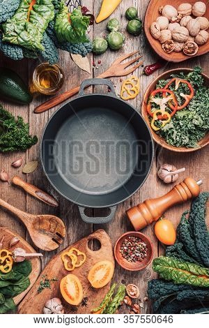 Various Organic Vegetables Ingredients And Empty Iron Cooking Pot, Wooden Bowls, Spoons On Wooden Ba