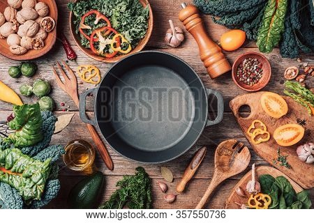 Various Organic Vegetables Ingredients And Empty Iron Cooking Pot, Wooden Bowls, Spoons On Wooden Ba