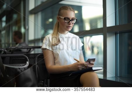 Female In Glasses And White Shirt Smart University Student Reading E-mail On Mobile Phone While Sitt