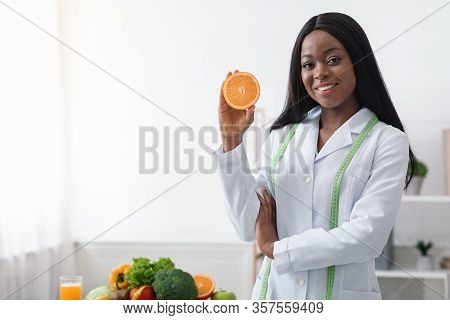 Start Your Day With Fresh Fruits. Positive Black Lady Nutritionist Holding Orange Half, Standing In 
