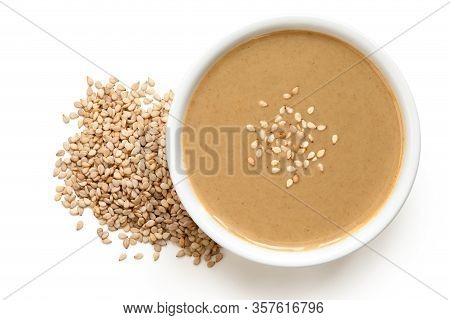 Tahini In A White Ceramic Bowl Sprinkled With Sesame Seeds Next To A Pile Of Sesame Seeds Isolated O