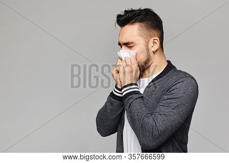 Young Sick Man Having Snotty Nose, Temperature And Feeling Bad. Sick Guy Has Sneezed, Isolated At Gr
