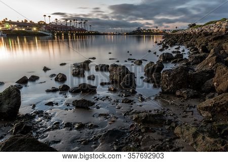 Scattered Rocks Reflec On The Calm Marina Water Surface As Storm Clouds Move Across The Morning Sky.