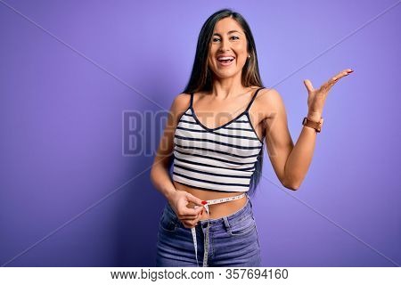 Young beautiful woman using measure tape on waist looking for healthy slim body very happy and excited, winner expression celebrating victory screaming with big smile and raised hands
