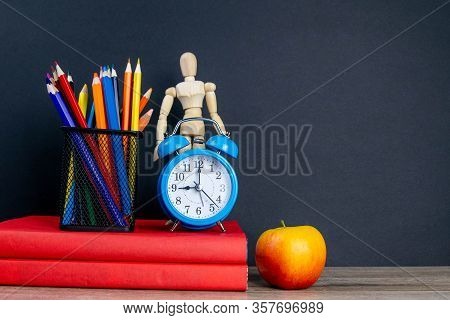 Two Red Books Stand On The Table, On The Books There Are Blue Watches And A Glass With Multi-colored