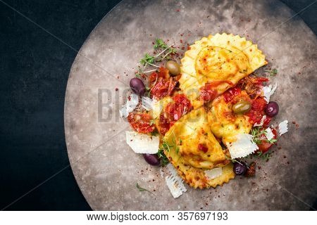 Traditional Italian ravioli pasta offered with parmesan cheese, fried tomatoes and olives as top view on a modern design plate with copy space left