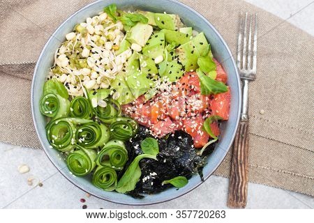 Salted Salmon Poke Bowl With Avocado, Sea Cale, Cucumber, Sesame Seeds And Bean Sprouts On Grey Back