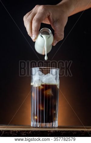 Iced Latte With Dark Background On A Wooden Table. Milky Iced Coffee. Pouring Milk Into Iced Espress