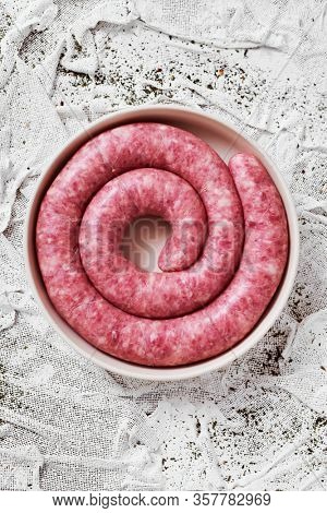 high angle view of a rolled botifarra, a pork meat sausage typical of Catalonia, Spain, in a plate, on a white textured textile background