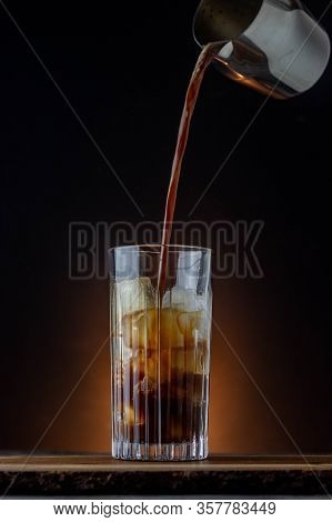 Iced Coffe With Dark Background On A Wooden Table. Coffee Pouring On Ice.