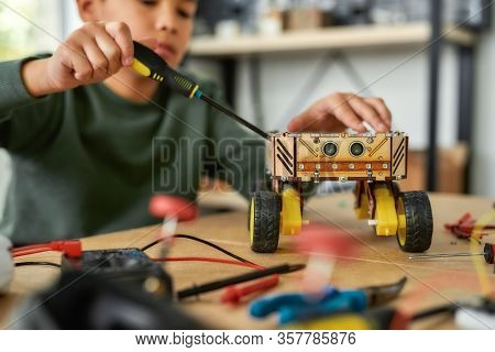 Close Up Of A Boy Using Screwdriver While Fixing Bolts On A Robot Vehicle. Smart Kids And Stem Educa