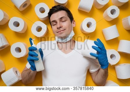 Calm And Happy Young Man With Medical Face Mask Surrounded By Toilet Paper Holding Hand Sanitizing G