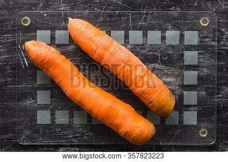 Top View Of Two Unpeeled Carrots On Glass Cutboard Before Peeling On The Black Background