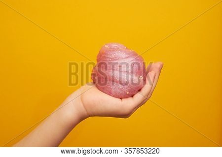 Pink Slime With Sequins, In A Childs Hand, On A Yellow Background. Creativity, Creativity And Experi