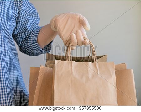 Courier In A Checkered Blue Shirt With Medical Latex Gloves Safely Delivers Online Purchases In Brow