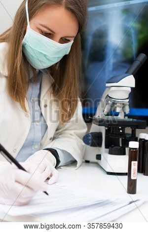 Scientist In Medical Mask In Laboratory. Pneumonia X-ray Film On Background.