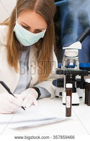 Scientist In Medical Mask In Laboratory. Pneumonia X-ray Film On Background.