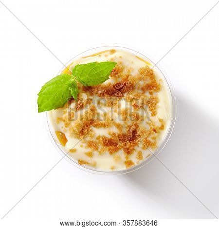 Dessert with mango, vanilla cream and cookie crumbs in restaurant glass isolated. Delicious fruit blancmange with apricots, prepared panna cotta or creamy mousse on white table closeup