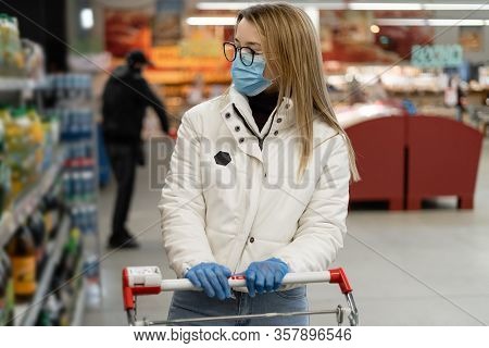 Young Woman Buys Goods In A Store. Panic Buying Of Goods In Supermarkets. A Mask On The Face Of A Gl
