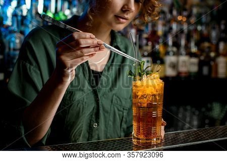 Young Woman Using Tweezers Gently Decorates Cocktail By Glass Sticks