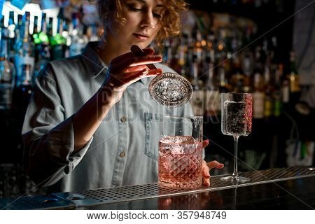 Young Womans Hand Holds Strainer Over Large Glass With Pink Drink