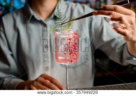 Close-up Young Woman Barman Decorates Glass With Rose Cocktail By Piece Of Green Plant.