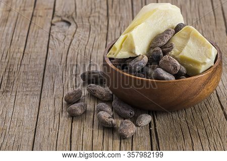 Cocoa butter or Cocoa bean solid oil with cacao powder in spoon or bowl and raw cocoa beans on rusti