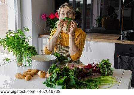 Playful And Funny Blonde Woman Holding Sprout Onion Like Mustache. Humorous Cooking Of Mixed Eco Veg
