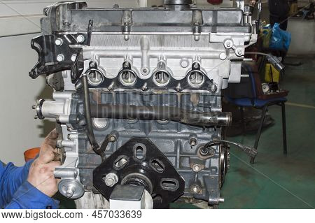 A Mechanic In A Blue Uniform Installs A Pulley On The Crankshaft Of An Automobile Internal Combustio