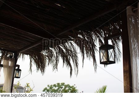 Lamp Hanging From A Wooden Pole. Jute Ceiling With Palm Leaves.evening Picture With Black Rectangula