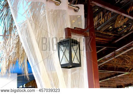Lamp Hanging From A Wooden Pole. Jute Ceiling With Palm Leaves.evening Picture With Black Rectangula