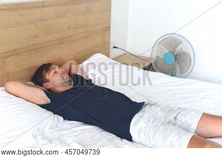 Young Man Laying And Sleeping Against Fan On A Hot Summer Day