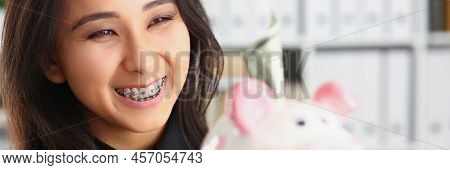 Portrait Of Pretty Laughing Young Woman Holding Piggybank With Banknote In It. Smiling Brunette Fema