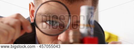 Close-up Of Businessman Holds In Hand Black Magnifying Glass Looks At Tower Of Coins Placed On Woode