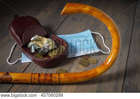 Money Spilling From An Open Purse Onto A Wooden Table With Cane And Surgical Mask Alongside Viewed F