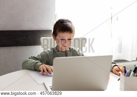 A Schoolboy Boy Sits At A Table In Front Of A Laptop And Studies Dma. Distance Learning For Children